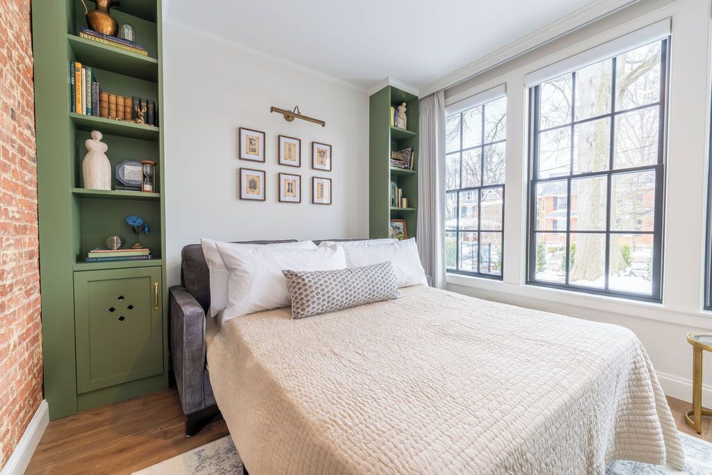 Un dormitorio con una cama grande, estanterías verdes y vistas amplias a través de grandes ventanales.