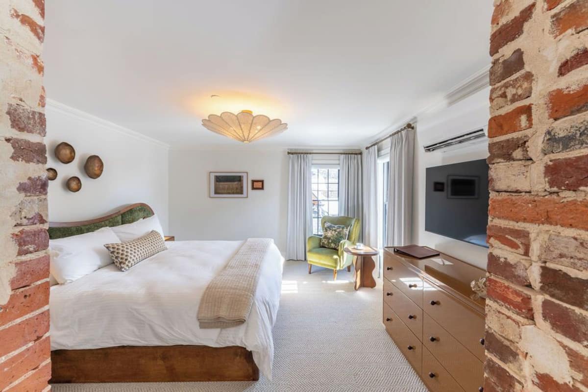 A bedroom with a bed, a green armchair, a dresser, and a TV.