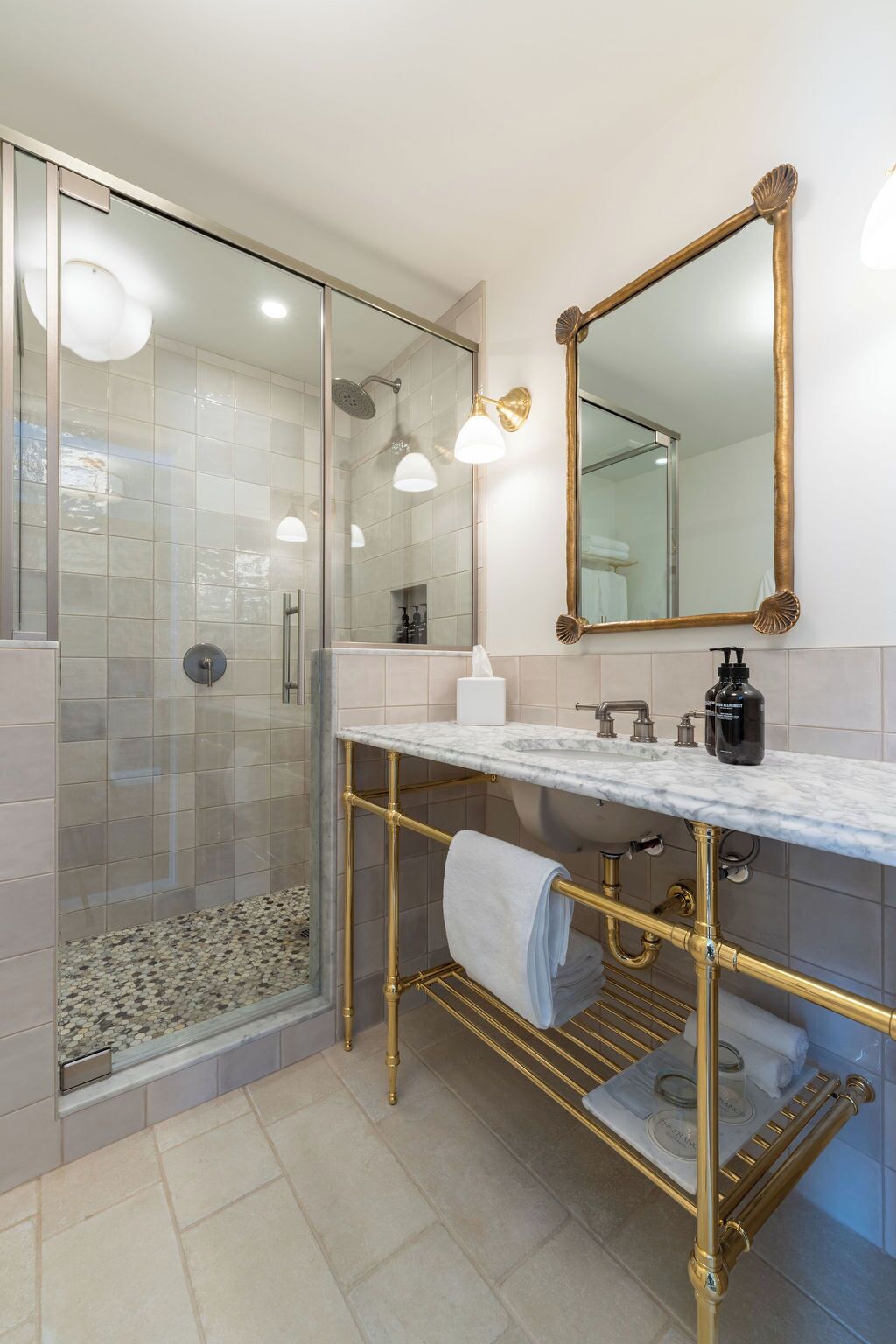 A modern bathroom with a glass-enclosed shower, a marble countertop, gold fixtures, and a large mirror.