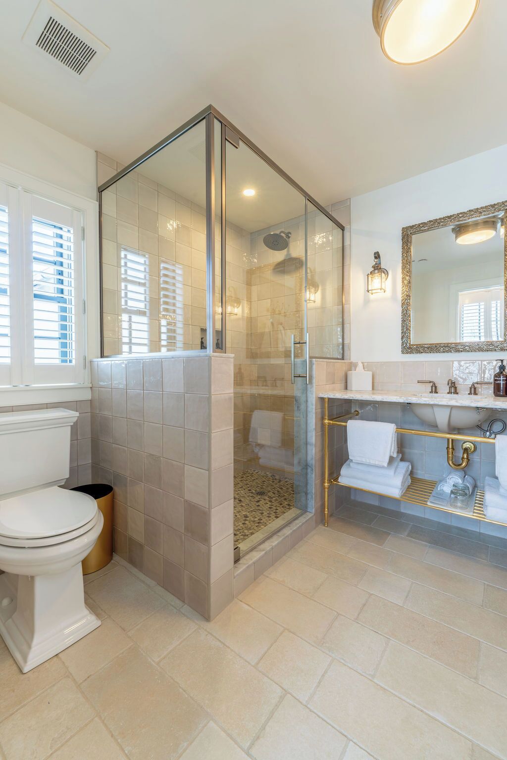 A modern bathroom with a glass-enclosed shower, a white toilet, and a vanity with a gold frame.