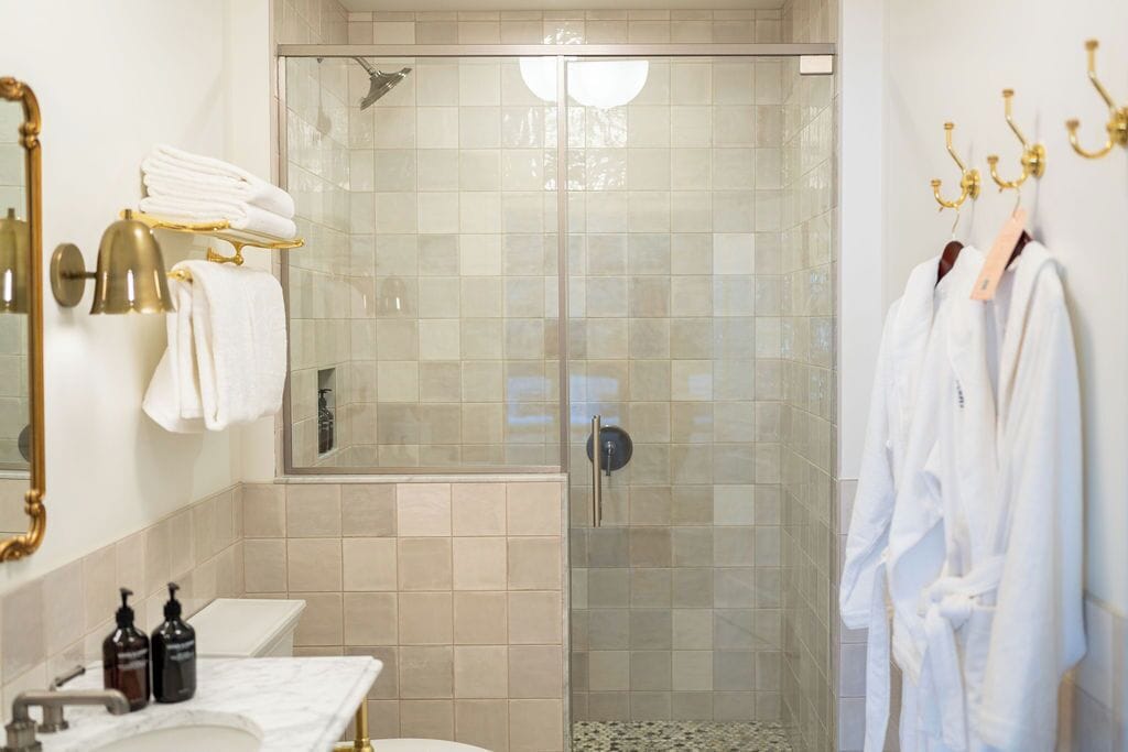 A modern bathroom with a glass-enclosed shower, a vanity with a marble countertop, and a gold mirror.