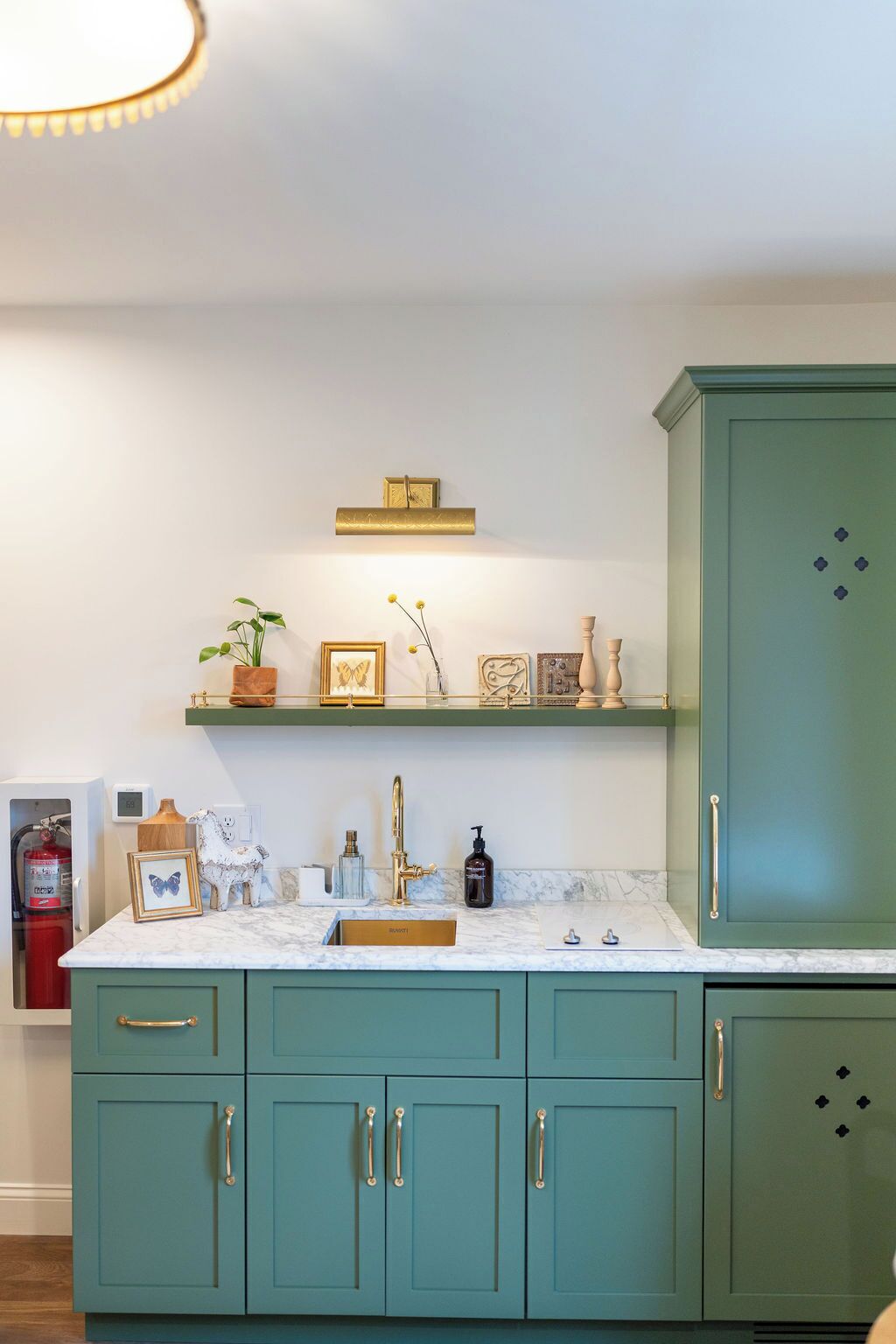 Une cuisine avec des armoires de couleur turquoise, un plan de travail en marbre et une étagère ornée d’objets décoratifs.