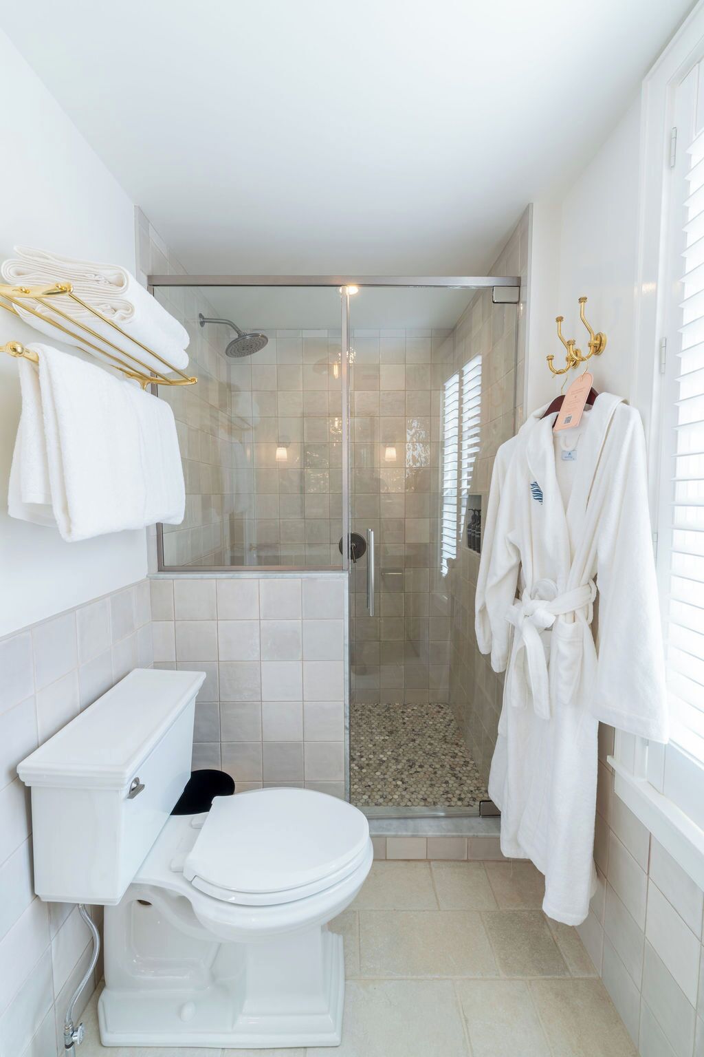 Un baño moderno con ducha envuelta en vidrio, inodoro y una bata colgada en un perchero.