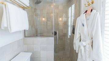 Un baño moderno con ducha envuelta en vidrio, inodoro y una bata colgada en un perchero.