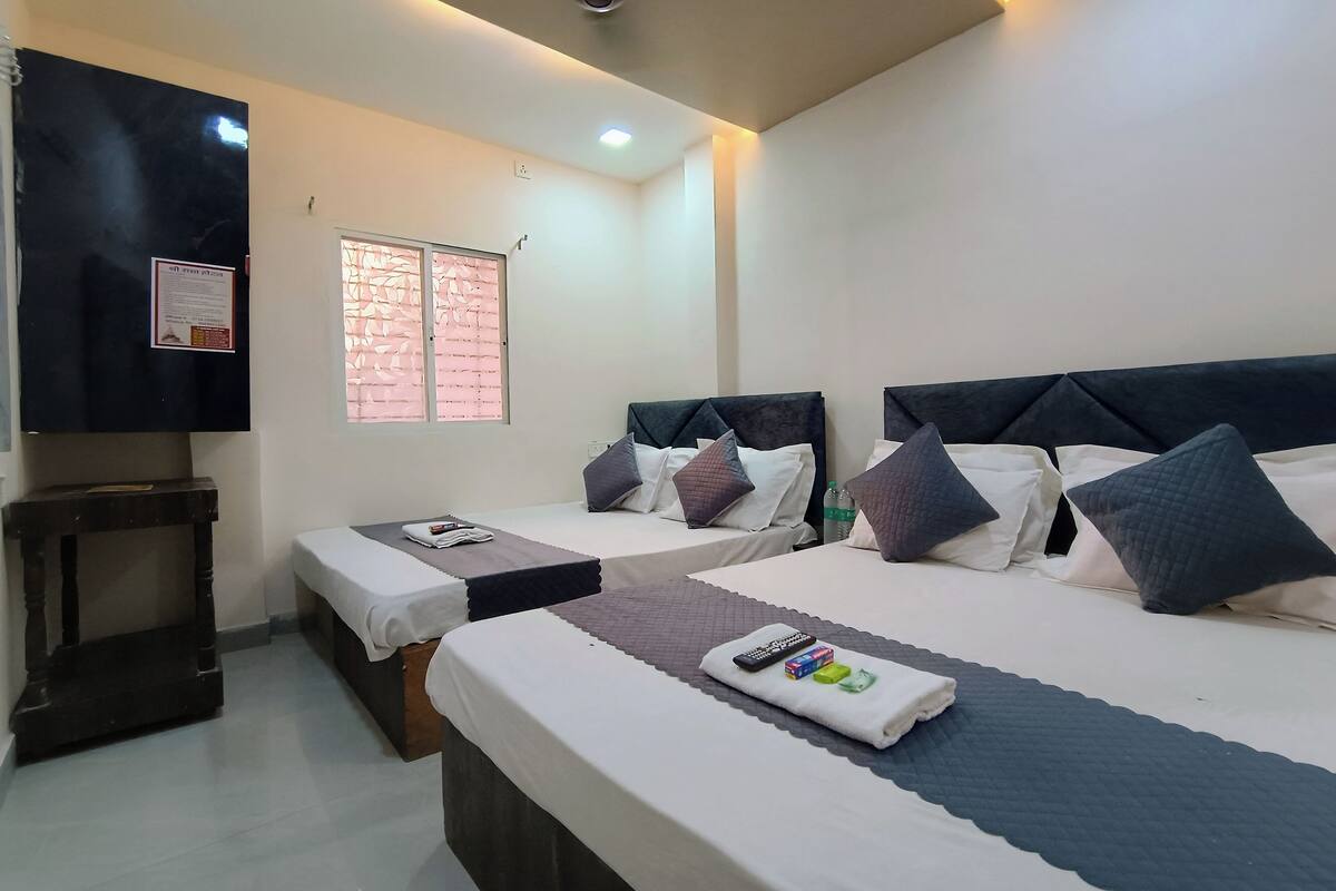A hotel room with two beds, a small table, a TV, and a window with blinds.
