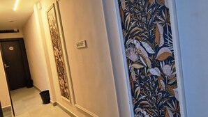 A hallway with a tiled floor, a door with a number sign, and a wall with a floral pattern. - Shri Radha hotels (Ujjain)