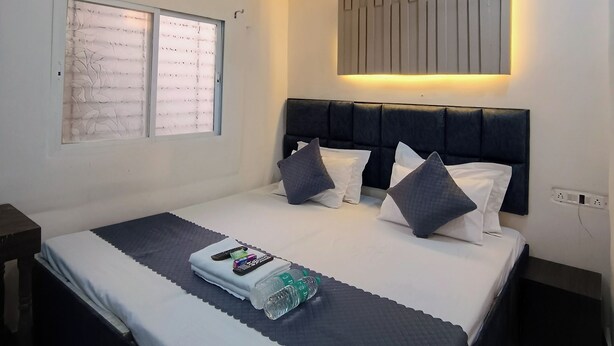 A modern bedroom with a bed, bedside tables, a ceiling fan, an air conditioning unit, and a wall-mounted light fixture. - Shri Radha hotels (Ujjain)