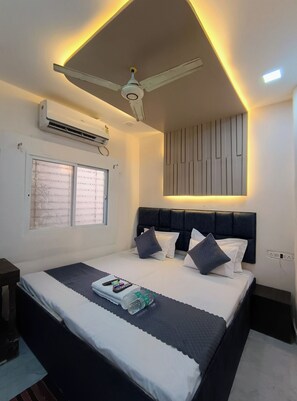 A modern bedroom with a bed, bedside tables, a ceiling fan, an air conditioning unit, and a wall-mounted light fixture. - Shri Radha hotels (Ujjain)