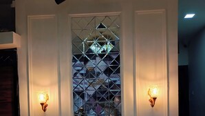 A room with a large window featuring a geometric pattern, two wall-mounted lights, a ceiling-mounted security camera, and a wooden cabinet. - Shri Radha hotels (Ujjain)