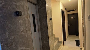 A hallway with marble walls and a tiled floor, leading to a door marked with a number. - Shri Radha hotels (Ujjain)