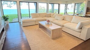 Una sala de estar moderna con un sofá seccional grande, una mesa de centro de madera y vista al océano a través de ventanas amplias.