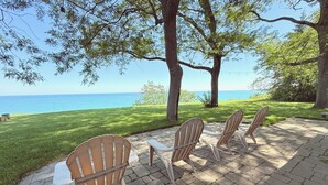 Un patio con cuatro sillas Adirondack y una mesita, con vistas a un espacio verde y al océano.