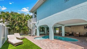 A pool area with a covered patio, two lounge chairs, and a spiral staircase.