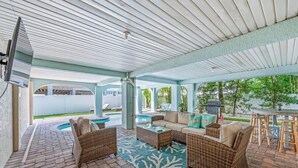 An outdoor patio with wicker furniture, a pool, and a covered area with a TV.