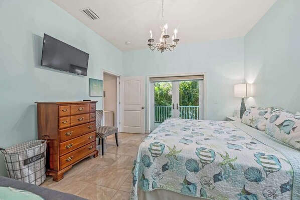 A bedroom with a bed, dresser, TV, and balcony doors.
