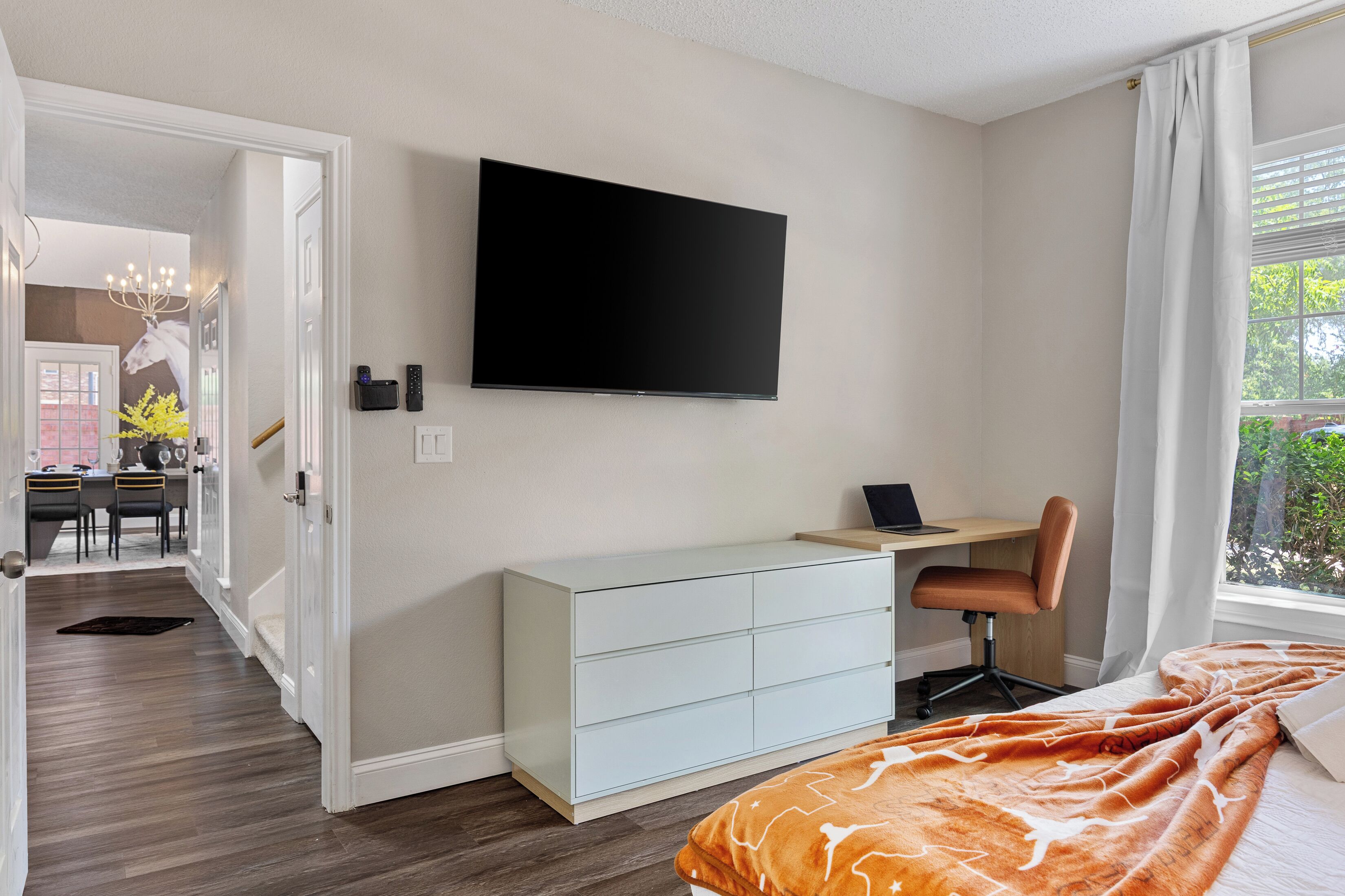 Une chambre à coucher avec un lit, un bureau avec une chaise, une télévision et une fenêtre avec des rideaux.