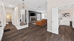A spacious living area with a fireplace, a sofa, and a kitchen with white cabinets. - The Pony Haus – Pool, Spa +Climbing Wall sleeps 11 in Frisco TX! (Frisco)