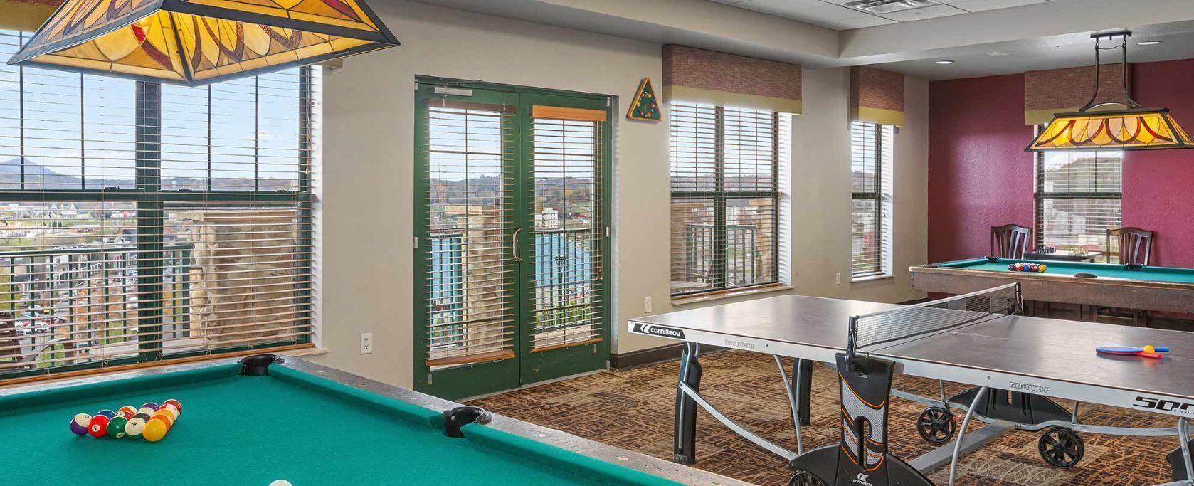 Une table de billard, des billes de billard et une table de ping-pong se trouvent dans une pièce dotée de grandes fenêtres et offrant une vue sur la ville.