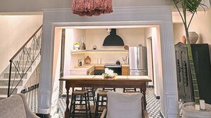 Uma sala de estar com um lustre grande e texturizado, uma área de jantar e uma cozinha ao fundo, além de um piso estampado.