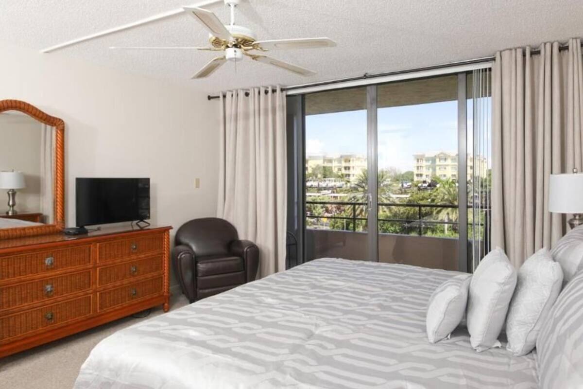 A hotel room with a large bed, a dresser, a television, a chair, and a balcony with a view.