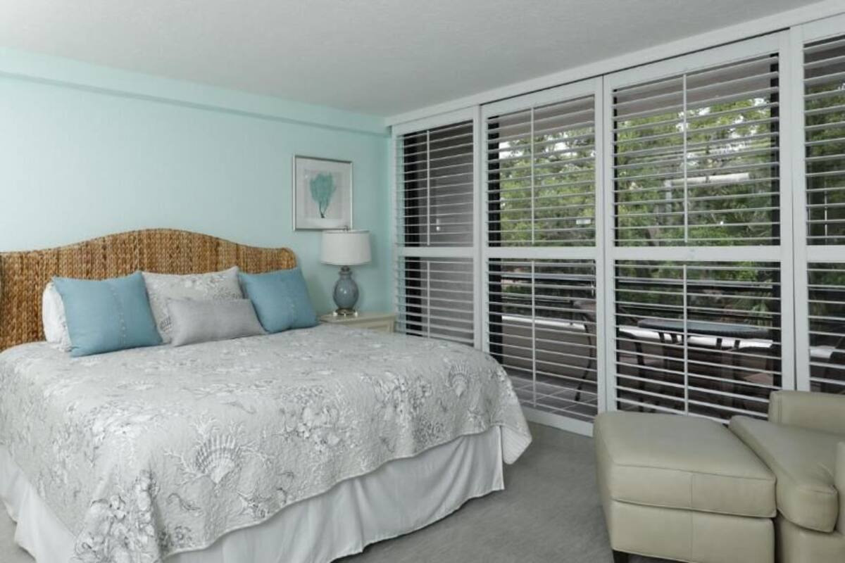A bedroom with a large bed, a bedside table, a lamp, and a window with blinds.
