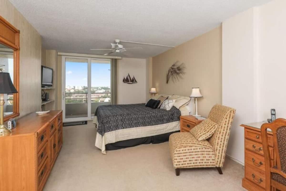 A bedroom with a bed, a chair, a dresser, a television, and a ceiling fan.