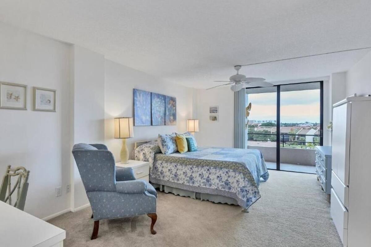 A bedroom with a bed, a chair, a desk, and a window with a view.