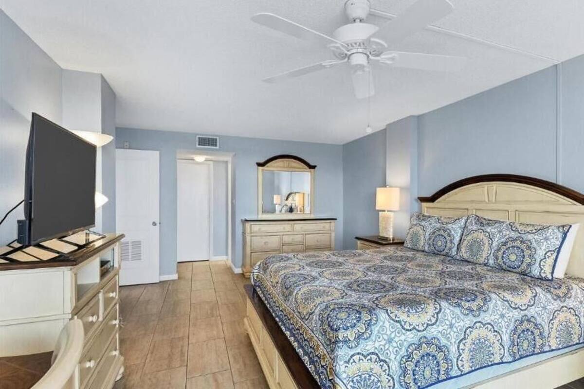 A bedroom with a bed, a dresser, a TV, a ceiling fan, and a door.