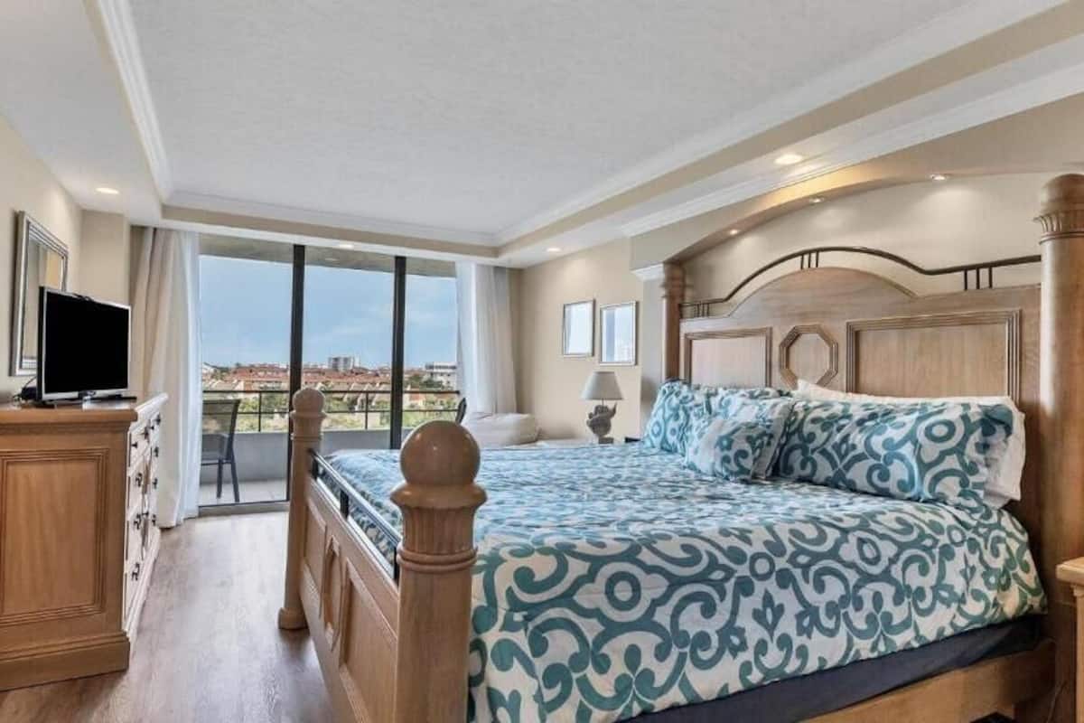 A spacious bedroom with a large bed, a television, and a balcony with a city view.
