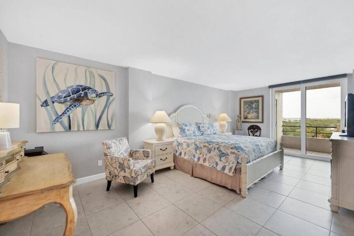 A bedroom with a bed, a chair, a nightstand, a lamp, and a painting of a sea turtle.