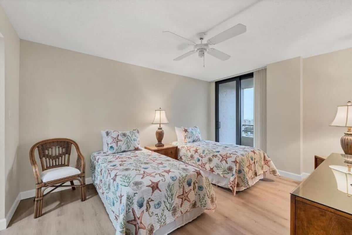 A bedroom with two beds, a ceiling fan, a chair, and a nightstand with a lamp.