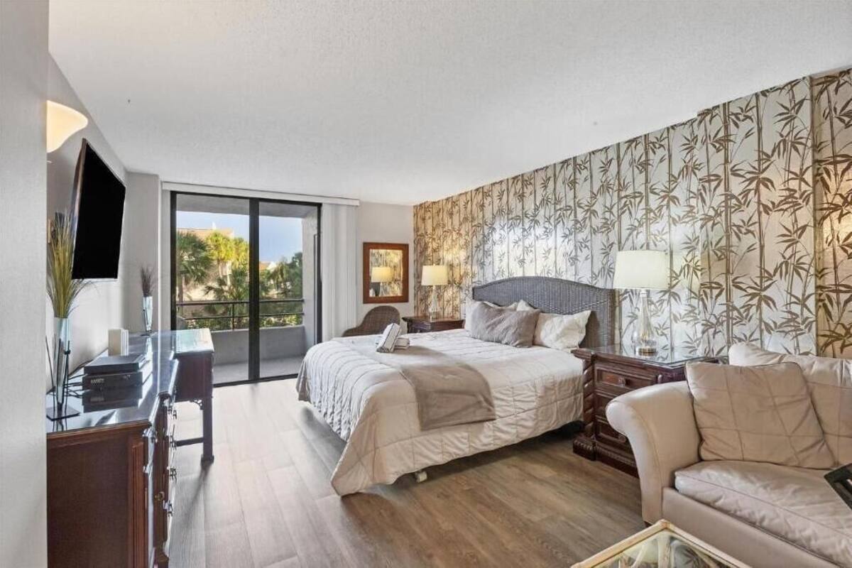 A hotel room with a large bed, a desk, a sofa, and a balcony with a view.