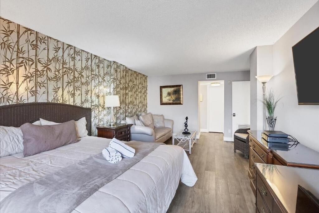 Una camera da letto con un letto grande, un comodino con una lampada, una sedia, una scrivania con una lampada e una porta che dà su un'altra stanza.