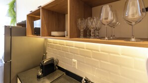 Una cocina con estantes de madera, salpicadero de azulejos blancos y una cafetera.