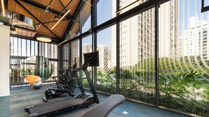Un gimnasio con equipo de ejercicio, ventanas amplias y vistas de edificios altos.