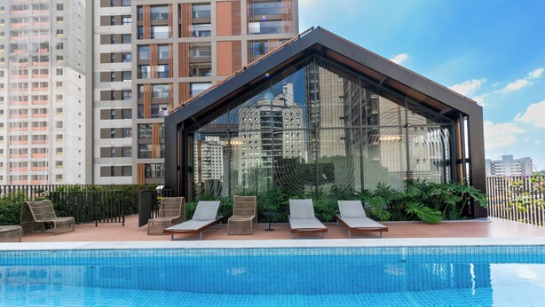 Un edificio moderno con fachada de vidrio, piscina y sillones de descanso.