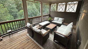 A covered porch with wicker furniture, a ceiling fan, and large windows overlooking a forest. - Model- Home Modern, Spacious, and Great Location (Buford)
