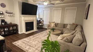 A living room with a fireplace, a large sofa, a coffee table, and a television. - Model- Home Modern, Spacious, and Great Location (Buford)