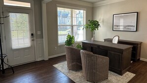 A spacious room with a wooden desk, wicker chairs, a potted plant, and a framed picture on the wall. - Model- Home Modern, Spacious, and Great Location (Buford)