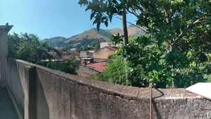 A narrow alleyway with a concrete wall on one side and a building on the other. There are two trash bins and a metal gate in the alley. - Village Apartment Building (Rio de Janeiro)