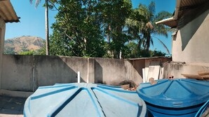 A narrow outdoor corridor with concrete walls and a tiled floor, leading to a small enclosed area with a blue umbrella and a water tank. - Village Apartment Building (Rio de Janeiro)