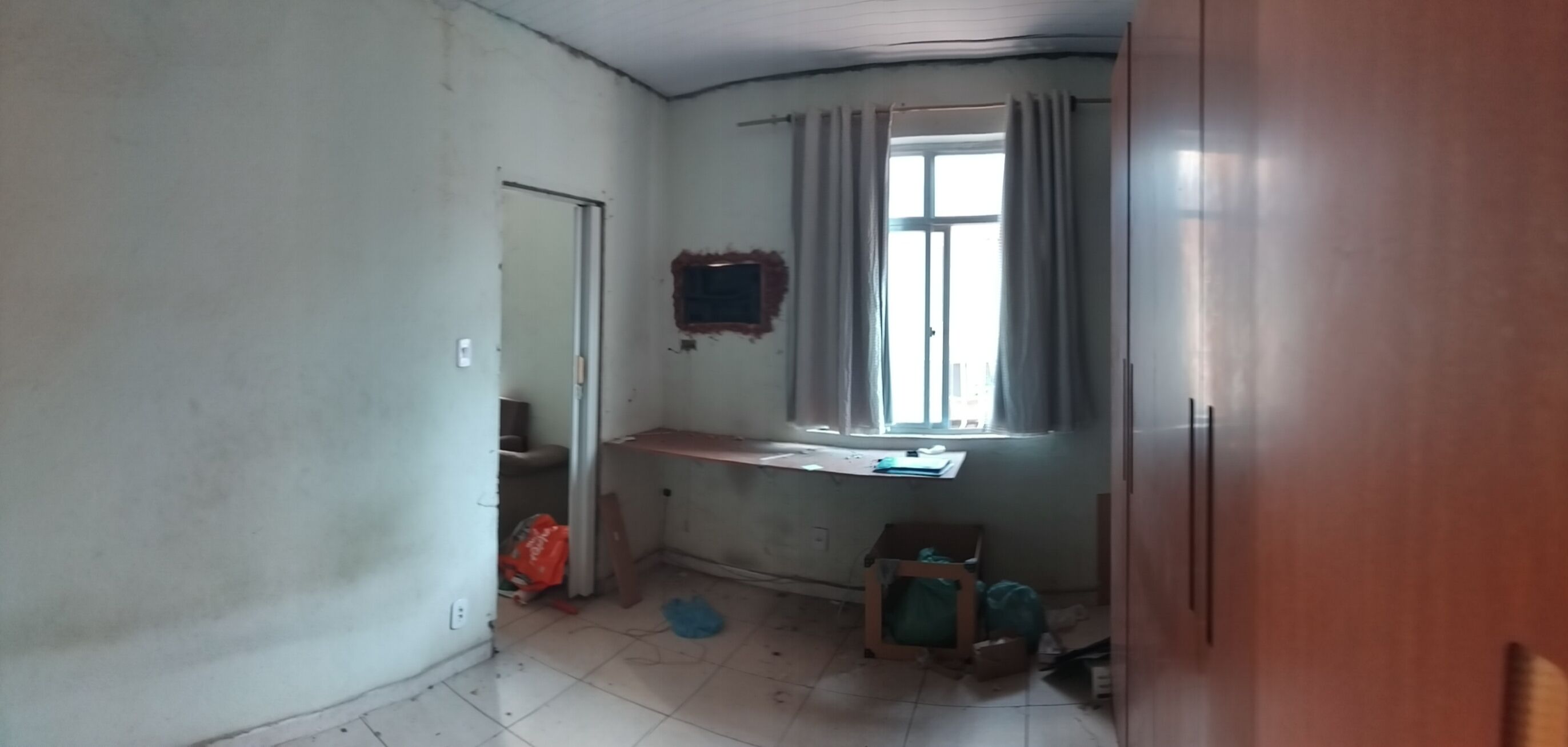 Ein kleiner, schwach beleuchteter Raum mit einem Fenster, einem Schreibtisch und einem Stuhl.