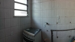 A kitchen with white tiled walls, a stove, and a window. - Village Apartment Building (Rio de Janeiro)
