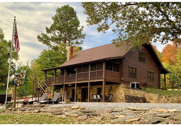 A rustic log cabin with a balcony, stone foundation, and a flagpole. - Log cabin with walkout basement and loft located on Ohio River’s edge. (Smithland)