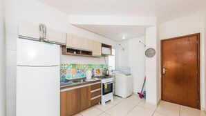 A compact kitchen with a refrigerator, stove, microwave, and a washing machine. - Cozy Apartment near Cambirela CFT (Palhoça)