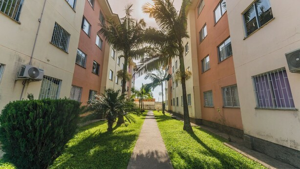 A courtyard with a central pathway flanked by buildings with barred windows and air conditioning units. - Cozy Apartment near Cambirela CFT (Palhoça)