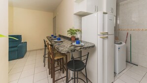 A compact kitchen with a built-in refrigerator, a dining table with chairs, and a potted plant. - Cozy Apartment near Cambirela CFT (Palhoça)