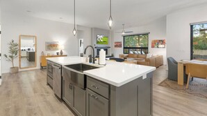 Une cuisine moderne dotée d’un îlot central, d’appareils électroménagers en acier inoxydable et de luminaires suspendus.