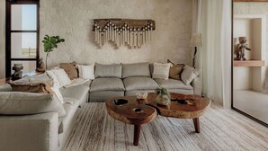 A living room with a stone wall, a grey sofa, two wooden coffee tables, and a hanging macrame piece.