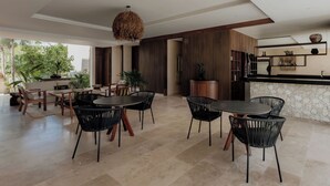 A spacious dining area with a round table and chairs, a hanging light fixture, and a kitchen area with a stone countertop. - Oceanfront Escape – Two-Level Penthouse with Private Rooftop & Pool (Tulum)
